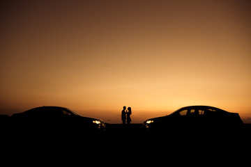 Fototapeta premium Loving couple enjoying full of love during lovely summer sunset with their same cars, love concept