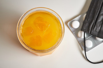 Glass of fresh orange juice, mask and pills. Top view. Brown background.