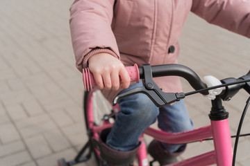 Fototapeta na wymiar The child is holding the wheel of a bicycle. A girl in a pink jacket is riding her bike.