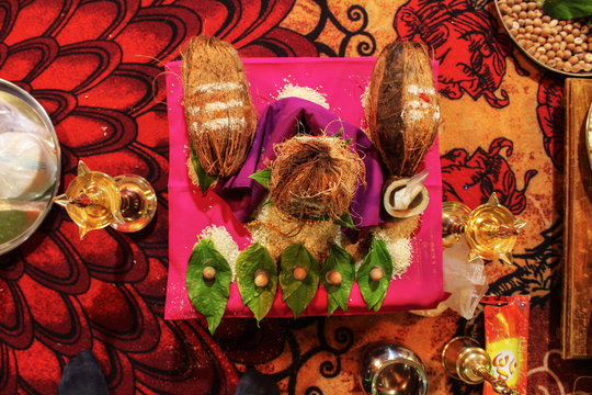 Stock photo of Indian hindu wedding rituals, small wooden stool cover with pink color cloth, peeled coconut kept on copper pot decorated with flowers, betel leaf, rice, betel nut , turmeric etc.