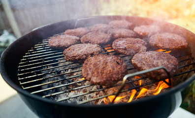 Smoking burgers being cooked on a barbecue grill with flames coming off the charcoal on a sunny day in the garden.