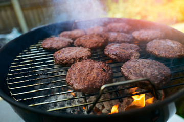Smoking burgers being cooked on a barbecue grill with flames coming off the charcoal on a sunny day in the garden.