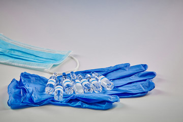 Seven mockup ampoules with transparent liquid on blue disposable gloves and medical mask isolated...
