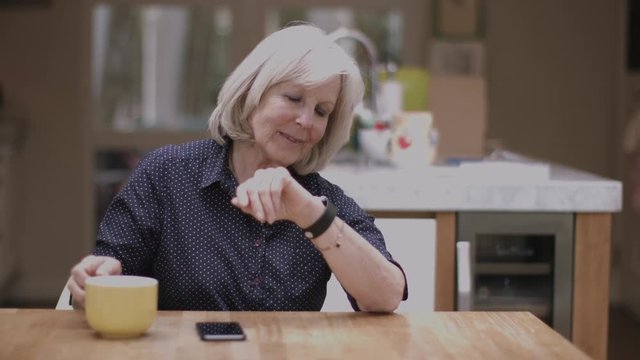 Senior Adult using smart watch at home on kitchen table