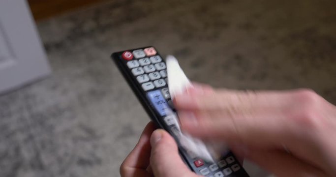 A closeup view of a man cleaning his television remote control with a disinfectant wipe. Cleaning commonly touched surfaces was a common procedure to help flatten the curve in the COVID-19 pandemic.  