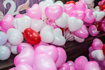 A large number of inflated multicolored heart-shaped balloons are stacked in bulk in the corner of the room for the upcoming holiday, close-up, copy space.