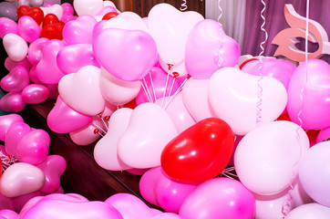 A large number of inflated multicolored heart-shaped balloons are stacked in bulk in the corner of the room for the upcoming holiday, close-up, copy space, toned.