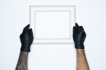 A man hand with black gloves holding a empty(blank) white photo frame isolated on white background.