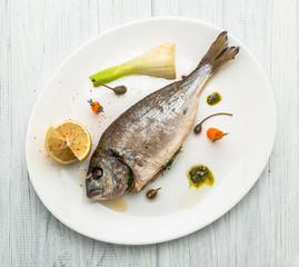 Grilled fish on platter isolated on white. Top view of whole roasted dorado