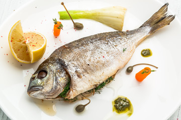 Grilled fish on platter isolated on white. Top view of whole roasted dorado