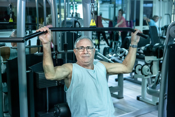 Uomo anziano si allena in palestra ai macchinari con un esercizio per i dorsali