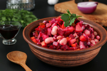 Traditional Russian salad vinaigrette with beans, pickles and boiled vegetables in a clay bowl against a dark background, Vegetarian food