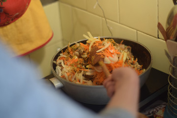 Woman stirs vegetables with a wooden spoon in a pan in the kitchen