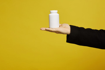 A white bottle of drugs on a male palm on yellow background, isolated with copy space. Healthcare concept. Prevention infection, viruses and seasonal illness.