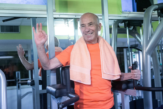 Uomo anziano con maglia arancione e asciugamano al collo  si allena in palestra nei macchinari, 