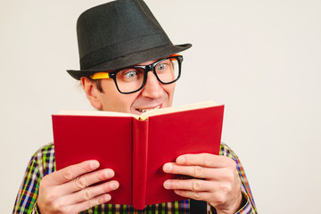 Nerd guy reading book at home. Man wears retro hat. Amazed nerd with red book. Home leisure concept.