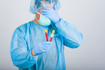 Doctor in medical uniform with a protective face mask and a gloved hand holding two test tubes with blood for 2019-nCoV analyzing. Novel Chinese Coronavirus blood test Concept.