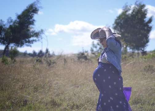 Mujer joven embarazada con sombrero de paja y vestido azul caminando en el prado 
