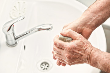 Senior elderly man his hands with soap under tap water faucet, detail photo. Can be used as hygiene illustration concept during coronavirus / covid-19 outbreak prevention