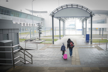 Mother and daughter with Luggage go to the entrance to the airport. View from the back. Quarantine in an empty terminal. The family is returning from a trip.