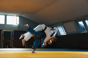 Two young judo caucasian fighters in white and blue kimono with black belts training martial arts...