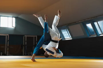 Gordijnen Two young judo caucasian fighters in white and blue kimono with black belts training martial arts in the gym with expression, in action, motion. Practicing fighting skills. Overcoming, reaching target © master1305