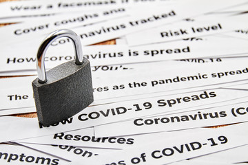 A closed padlock on the background of newspaper headline clippings. Coronavirus and travel concept. Closing borders between countries due to virus. Closeup