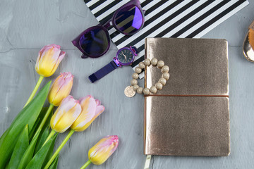 A gold notebook with women's shoes, tulips, glasses and a watch on a concrete background. Flet lay © Вася Фаевич