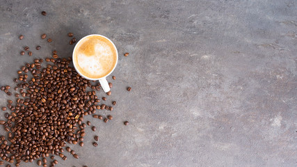 Cappuccino cup with milk foam and coffee beans on brown concrete background with copy space. Coffee time concept.