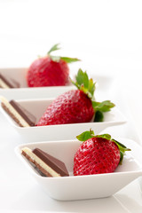 Three fresh red strawberries with chocolate in small white bowls