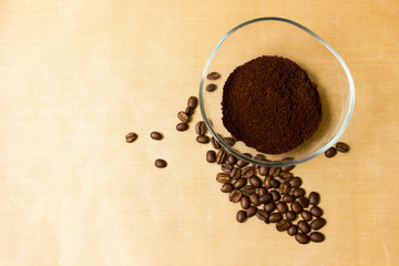 Coffee background. Natural roasted coffee beans and ground coffee in a glass transparent bowl on a natural beige fabric background, top view from Kopi space