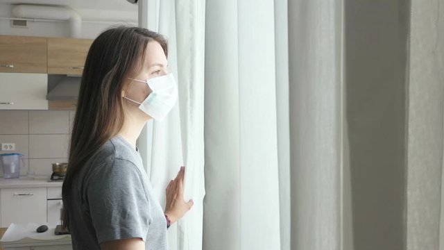 Woman in Face Mask Looking out the Window. Staying Home in Quarantine.