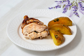 Roasted chicken breast, baked quarters of potatoes, sprinkled with parsley laid on a white plate