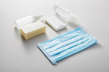 flat lay with hand sanitizer in spray bottles,  medical mask and antibacterial soap on grey background