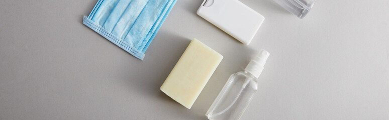 top view of hand sanitizer in spray bottles,  medical mask and antibacterial soap on grey background, panoramic shot