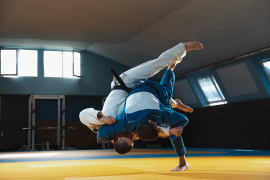 Two young judo caucasian fighters in white and blue kimono with black belts training martial arts in the gym with expression, in action, motion. Practicing fighting skills. Overcoming, reaching target