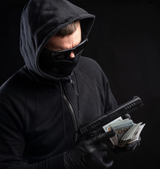 Man in black mask and hoody with a gun and pack of dollars