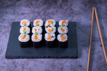 Set of maki rolls with salmon and avocado on concrete background and wooden chopsticks. Japanese cuisine.