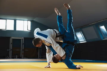 Fotobehang Two young judo caucasian fighters in white and blue kimono with black belts training martial arts in the gym with expression, in action, motion. Practicing fighting skills. Overcoming, reaching target © master1305