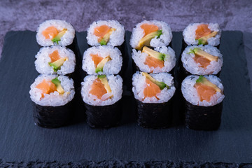 Salmon makis on a slate plate and concrete background. Japanese cuisine. Close up view.