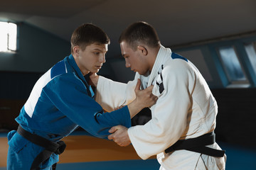 Two young judo caucasian fighters in white and blue kimono with black belts training martial arts...