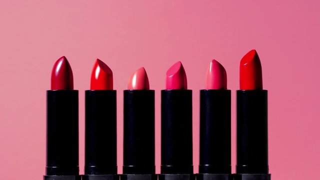 Stop motion video with a set of lipsticks in tubes, different colors of lipstick in the stick move up and down, pink background