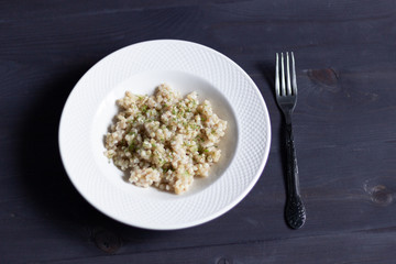 Cooked green buckwheat with dill in white plate with fork on black background 