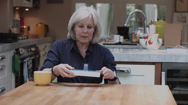 Senior Adult woman taking medicine at home in kitchen