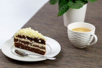 Dessert - chocolate cake with vanilla cream and white marzipan and white chocolate shavings on the dessert surface. In the background a white coffee cup.