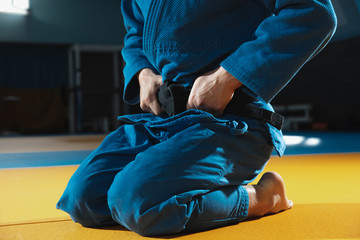 Young judo caucasian fighter in blue kimono with black belt posing confident in the gym, strong and...