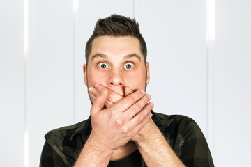 Young guy with beard close his mouth with his hands