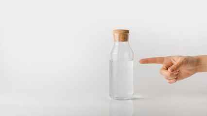 A hand points a finger at a glass bottle of clean water.