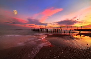 Fantastic sunset by the sea. Old iron pier and cormorant moon in pink clouds. Long exposure. Odessa. Black Sea. Ukraine.