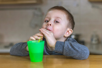 Portrait of beautiful little child in kitchen at home. Pretty boy drinks iced tea through a plastic straw in the kitchen.
